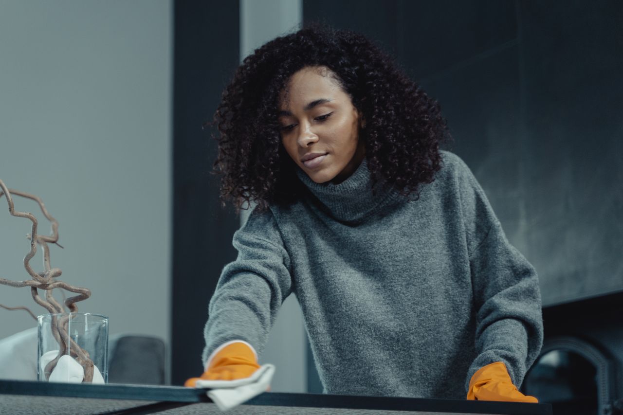 gallery-1 A woman wearing a gray sweater carefully wipes down a table, highlighting the ease and comfort of cleaning at home.
