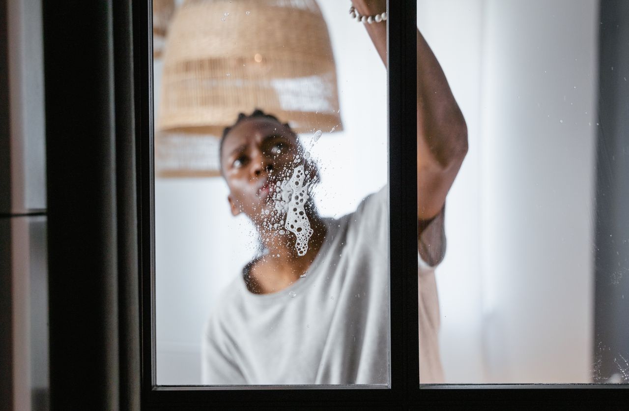 gallery-6 An adult male cleaning a glass window indoors, focusing on household chores and cleanliness.